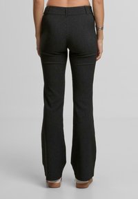 Černé pruhované rozšiřující se kalhoty s hladkým povrchem, vysokým pasem a minimálním švem, s detailem zadní kapsy.