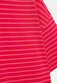 Tissu rouge avec des fines rayures horizontales blanches créant une surface textile lisse et pliée, montrant les détails de la texture et du motif.