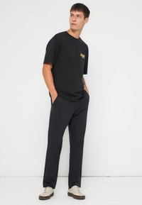Zwarte katoenen t-shirt met korte mouwen en een grafische print op de borst, gecombineerd met donkergrijze rechttoelopende broek en lichte casual sneakers.