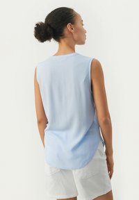 Hellblaues ärmelloses Top mit rundem Halsausschnitt, fließendem Stoff und leicht gewelltem Saum, kombiniert mit weißen Shorts.