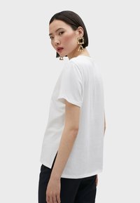 Camiseta blanca de manga corta con un corte relajado, aberturas en los costados y escote en forma de barco. La tela parece suave y ligera.