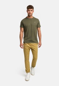 Olive green short-sleeve T-shirt paired with light yellow chinos and white sneakers. Simple design with a small logo on the chest.