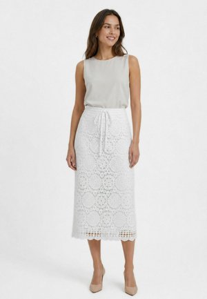 Donna che indossa un top senza maniche grigio chiaro infilato in una gonna midi bianca in pizzo con vita con coulisse e tacchi alti beige.