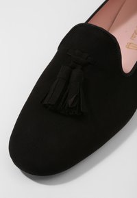 Mocassin en daim noir avec bout arrondi et doubles pompons sur le dessus, doté d'une doublure intérieure rose douce.