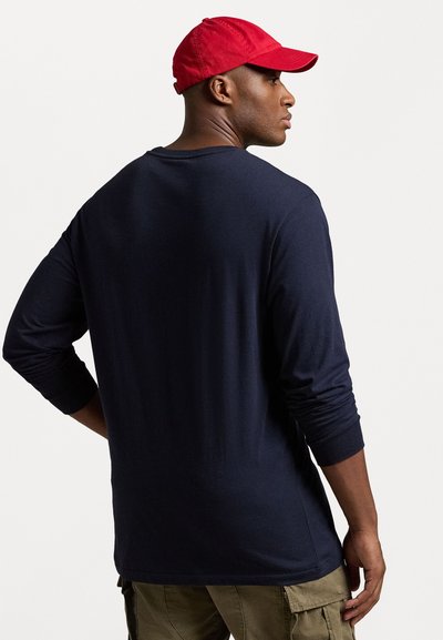 Marineblauw longsleeve T-shirt met een relaxed fit, voorzien van een ronde halslijn en gebreide manchetten, gecombineerd met een rode baseballpet.