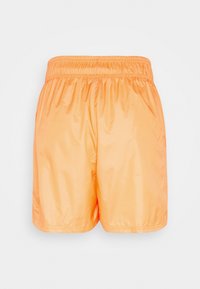 Shorts orange vif à taille élastique en tissu lisse légèrement brillant, vus de dos sur un fond neutre.