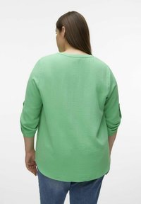 Haut en crêpe vert avec une coupe ample, des manches trois-quarts et une légère texture. Il dispose d'un col rond et tombe en dessous des hanches.