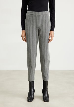 Vrouw draagt grijze slim-fit enkellange broek met een subtiel geruit patroon, zwarte top met lange mouwen en zwarte enkellaarzen.