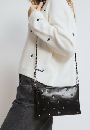 Black leather crossbody bag featuring silver star patterns, a zip closure, and a chain strap, worn alongside a white knit sweater.
