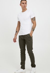 White short-sleeve t-shirt paired with olive green pants, featuring a slim fit and side pockets. Worn with white sneakers.