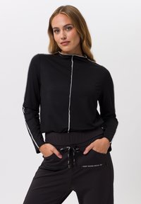 Black long-sleeve top with gray piping and a high neck, paired with black drawstring pants featuring side zippers and a print accent.