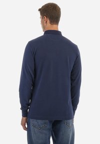 Marineblauwe polo met lange mouwen en een kraag, gemaakt van glad, lichtgewicht stof. Kenmerkt zich door een rechte zoom en geen zichtbare logo's of patronen.