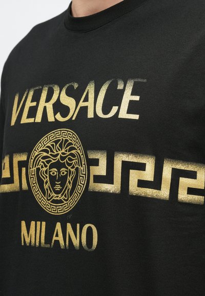 Černé bavlněné tričko s vytištěným zlatým nápisem "VERSACE MILANO" a středovým logem Medusa s akcentem řeckého klíče.