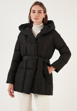 Doudoune noire avec capuche, texture matelassée, taille cintrée et manches longues. Présente une fermeture éclair et des poches latérales.