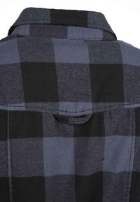 Camicia flanella a quadri nera e blu con colletto pieghevole, dotata di una chiusura con bottoni frontale e una tasca sul petto per un uso pratico.