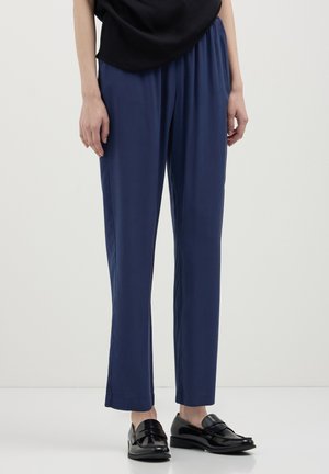 Pantaloni formali leggeri color blu navy con vestibilità comoda e vita elastica. Abbinati a mocassini neri lucidi. Texture liscia, design minimal.