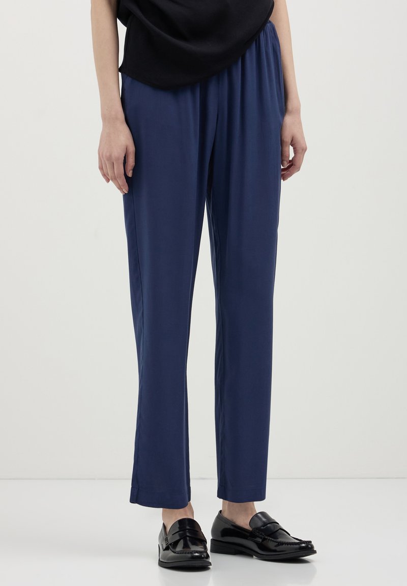Pantalons formels légers bleu marine, à coupe décontractée et taille élastique. Associés à des mocassins noirs et brillants. Texture lisse, design minimal.