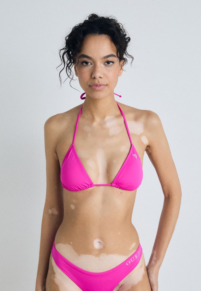 Roza bikini z večkotnim vrhom s tankimi trakovi in ujemajočimi se nizkimi hlačkami, poudarjenimi z logotipom na pasu.