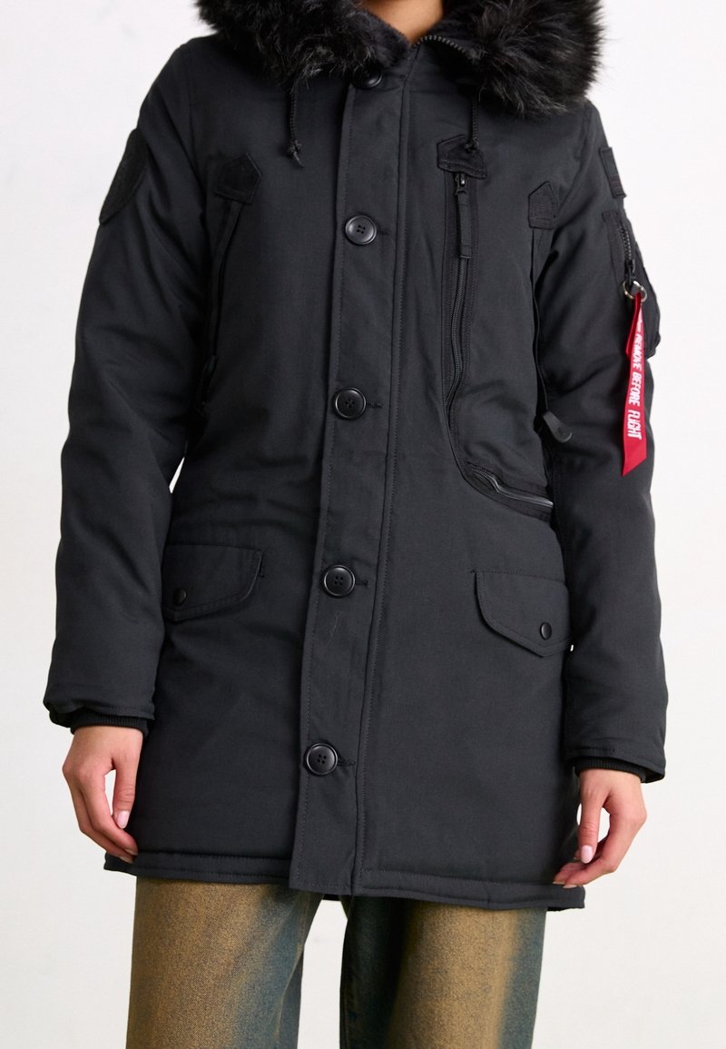 Svart parka-jacka med huva kantad med päls, dragkedja och knappstängning, två framsidor fickor och märke på ärmen. Mjuk tygkänsla.
