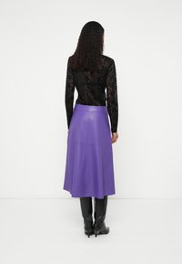 Violeta ādas A-līnijas svārki ar augstu vidukli un paneļu detaļām, kombinēti ar melnu mežģīņu garroku topu un melniem zābakiem līdz ceļiem.