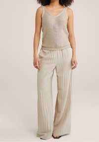 Beige paljett-topp med V-ringning och tight nederkant, matchad med ljusbeige vida byxor i en strukturerad tyg.