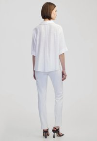 Weißes Hemd mit Kragen, kurzen Ärmeln und lockerer Passform. Kombiniert mit engen weißen Hosen und schwarzen High Heels. Glatte Stofftextur.