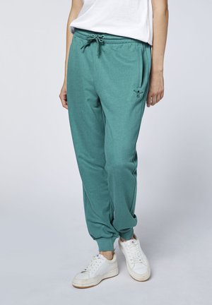 Person wearing teal jogger pants with drawstring waist, tapered cuffs, and white sneakers against a plain background.