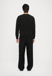 Pulover negru cu un model texturat, având manșete și tiv cu miller. Combinat cu pantaloni negri cu picioare largi și adidași albi. Vedere din spate.