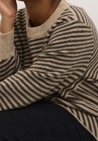 Pull rayé en tissu tricoté beige et brun foncé ; doté d'un col rond et d'une coupe décontractée, avec une texture visible et des fibres douces.