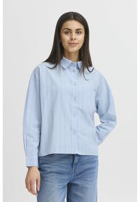 Světle modrá košile na knofl íky s vertikálními bílými pruhy, límcem, dlouhými rukávy a náprsní kapsou. Vyrobena z hladkého materiálu.