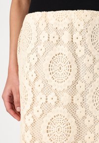 Spetskjol i krämvit med cirkulära och blommönster, med en texturerad stickad design och en åtsittande midja.