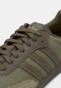 Green athletic shoe featuring a mesh upper with brown leather accents, tonal laces, and three horizontal stripes on the side.