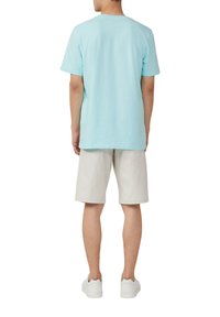 Lichtblauw katoenen T-shirt, korte mouwen, ronde hals, gecombineerd met beige shorts. Model draagt witte sneakers, gezien vanaf de achterkant.