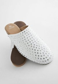 Vita klackskor utan hälar med en strukturerad ovandel prydd med runda rhinestones, bruna innersulor och rundade kanter för en bekväm passform.