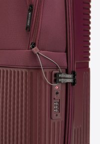 Valise rigide bordeaux avec texture rainurée, zips en métal, serrure à combinaison et accents de logo. Design compact adapté aux voyages.