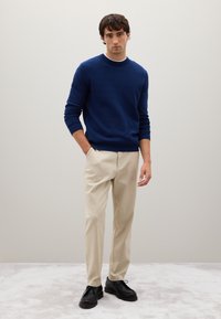 Maglione blu, pantaloni beige e scarpe nere. Il maglione ha un collo rotondo, polsini a coste e una vestibilità comoda. Tessuto dalla superficie liscia.