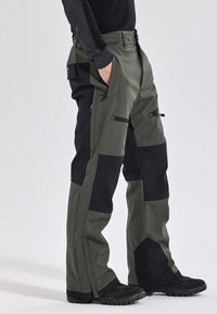 Mannen waterdichte broek in olijfgroen en zwart, met een ritszak, versterkte panelen en een losse pasvorm. Gemaakt van duurzaam materiaal.