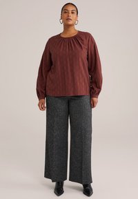 Top rojo texturizado con cuello gathered, acompañado de pantalones anchos grises. La ropa cuenta con mangas largas y un ajuste relajado. Botas negras hasta el tobillo.