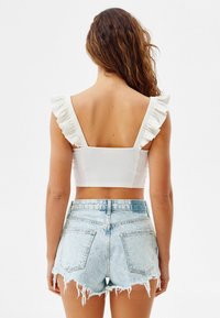 Vit ribbad crop top med volangband; matchad med bleka ljusblå denim shorts med fransade fållar och bakfickor.