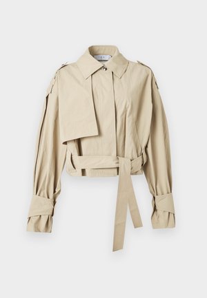 Trenci scurt bej, cu rever lat, talie cu curea, mâneci lungi cu barete la manșete și epoleți la umeri.