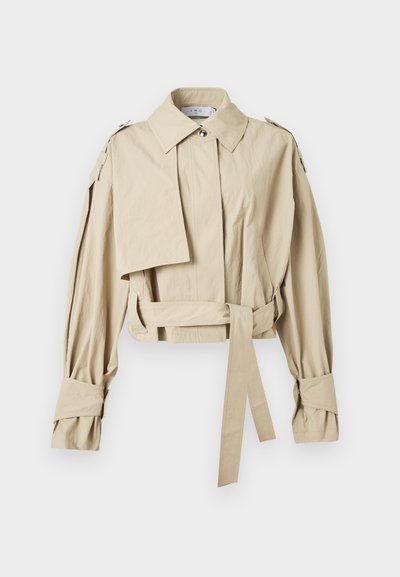 Μπεζ κοντό τρεντσκότ με φαρδιά γιακά, ζώνη στη μέση, μακριά μανίκια με λουράκια στα μανσέτα και επιτιράντες στους ώμους.