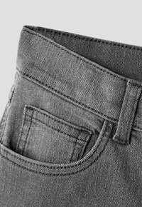 Close-up van grijze spijkerbroek met zicht op tailleband, ceintuurlus en voorzak met kleinere muntzakje erin.