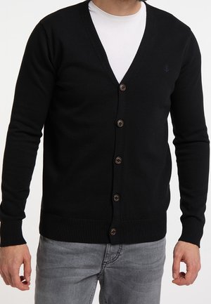 Schwarze, gestrickte Strickjacke mit V-Ausschnitt, sechs braunen Knöpfen und gerippten Bündchen sowie Saum. Über einem weißen T-Shirt getragen und mit grauen Jeans kombiniert.