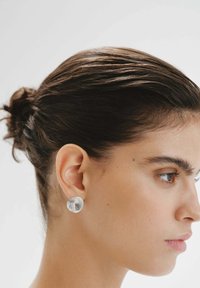 Pendientes circulares de plata con un diseño en espiral, que presentan una textura metálica suave. La imagen muestra una vista de perfil sobre un fondo neutral.