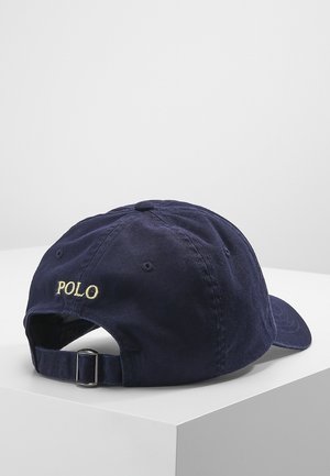 Marineblaue verstellbare Baseballkappe mit Metallverschluss und gelb gesticktem "POLO" auf der Rückseite, auf einer weißen Oberfläche platziert.