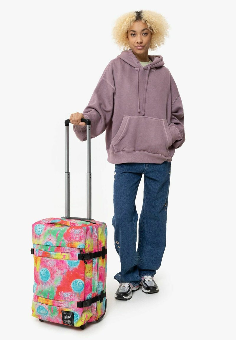 Maleta de mano con ruedas de diseño abstracto colorido en rosa, azul y amarillo; cuenta con correas negras y un mango retráctil.