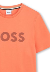 Koraalkleurig katoenen t-shirt met een groot bruin "BOSS" logo op de voorkant, met een ronde hals en korte mouwen. Glad textuur.