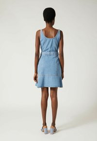 Lyhyt farkkumekko, jossa on vartalonmyötäinen yläosa, levenevä helma ja vyötärönauha. Vaaleansininen väri, näkyvät saumat ja hihaton malli.