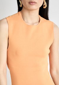 Oransje ermeløs topp i et glatt, elastisk stoff med rund halslinje. Har rene linjer og minimale sømmer, og gir en tettsittende silhuett.