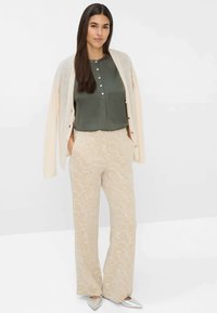 Blusa in raso verde con bottoni sul davanti, cardigan crema, pantaloni a palazzo beige con texture e ballerine argentate a punta.
